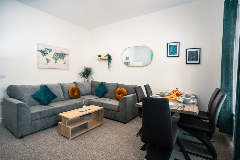 Modern living room with gray corner sofa, wooden coffee table, dining area, and wall art