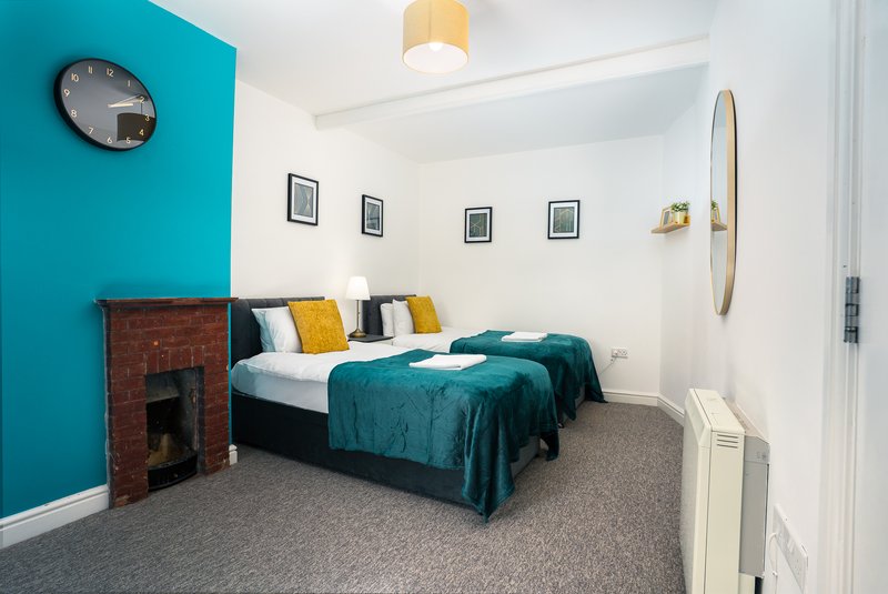 Bedroom with teal accent wall, double bed with teal bedding, fireplace and wall art