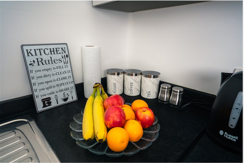 Modern kitchen counter with fruit bowl, storage containers, and decorative kitchen rules sign
