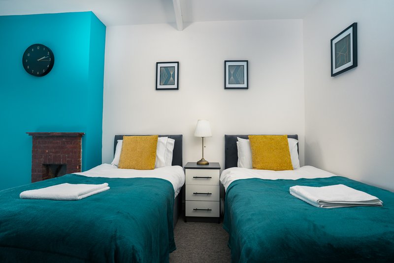 Twin bedroom with turquoise beds, yellow cushions, white bedside table, and framed wall art