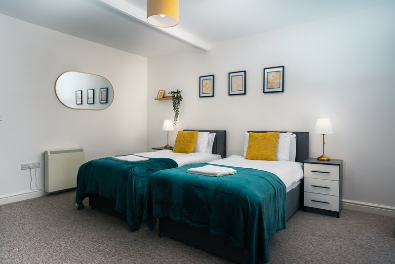 Modern bedroom with two single beds, teal bedding, yellow cushions, bedside tables and wall mirror