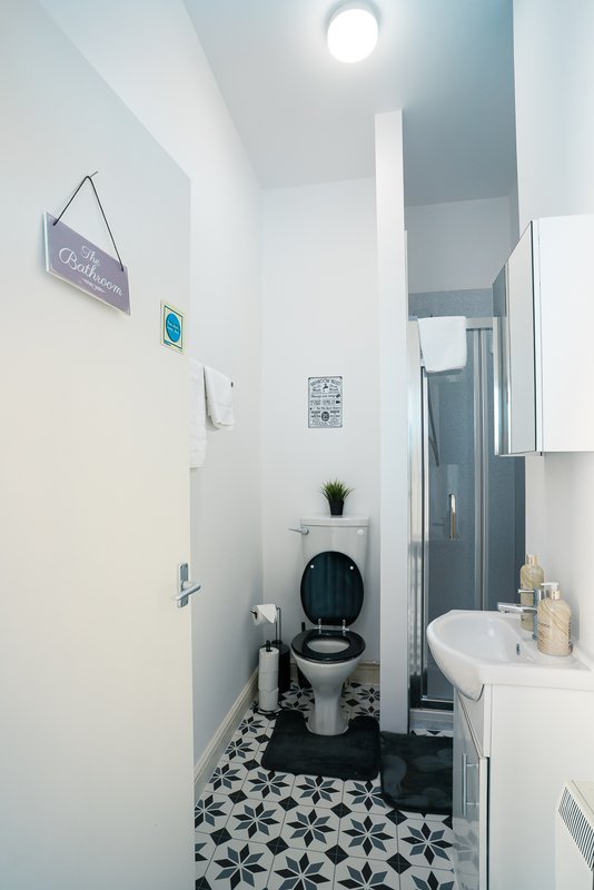 Modern bathroom with black and white tile floor, toilet, sink, shower enclosure and wall storage