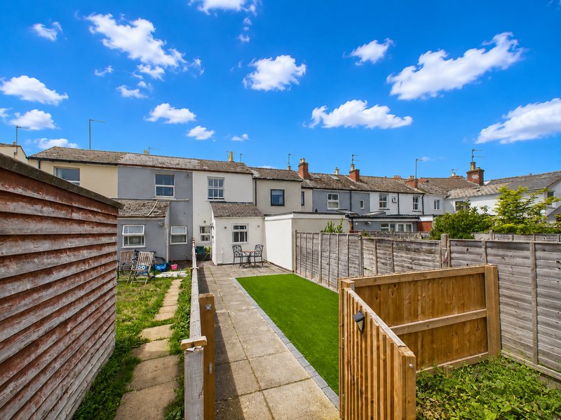 Rear garden with lawn, paved patio, wooden fences and adjacent terraced houses