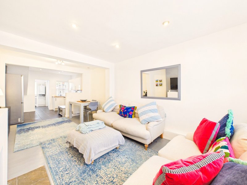 Bright open-plan living area with cream sofa, colorful cushions, and view to kitchen and bedroom