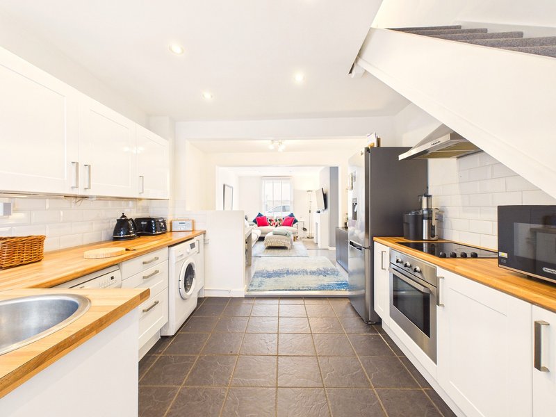 Modern kitchen with white cabinets, wooden countertops, appliances and open-plan living area beyond