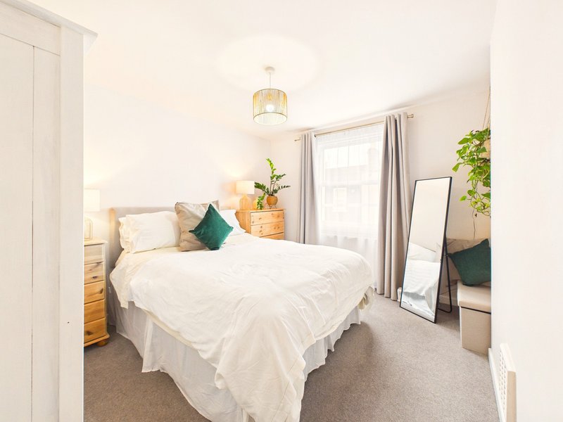 Bright bedroom with white bed, green cushion, wooden nightstands, mirror, and potted plants