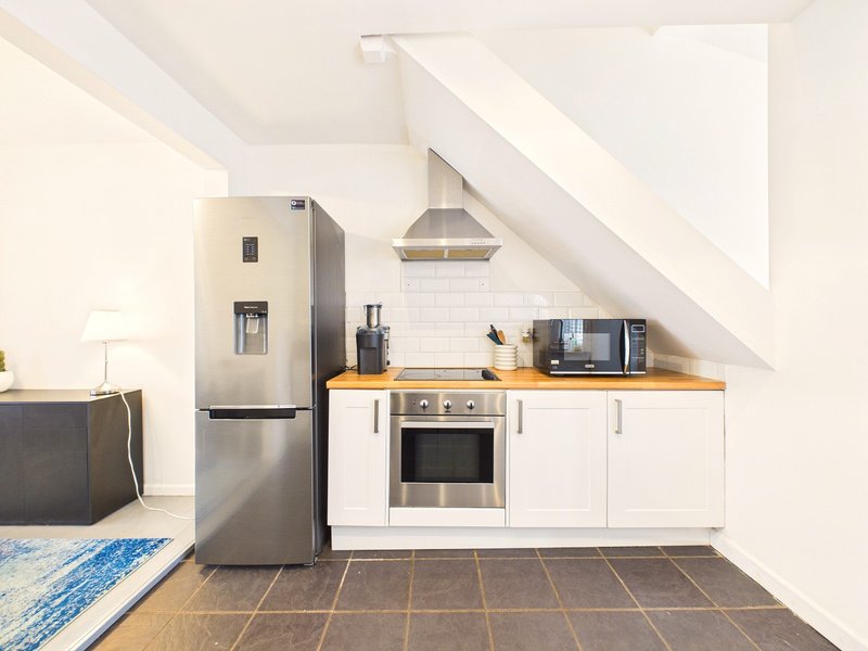 Modern attic kitchenette with stainless steel appliances, white cabinetry and sloped ceiling