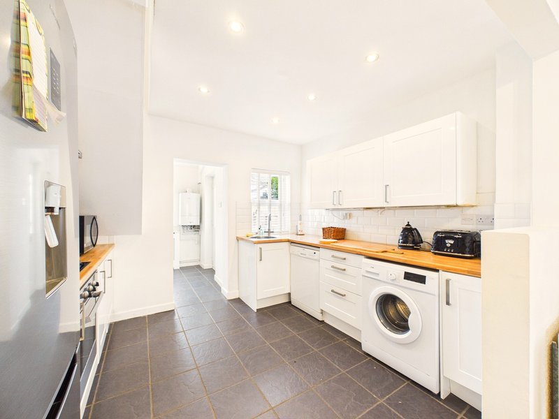 Modern kitchen with white cabinets, wooden worktops, washing machine and tile flooring