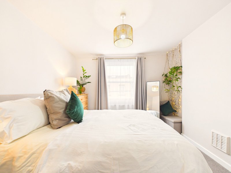 Bright bedroom with double bed, decorative pillows, pendant lamp, and potted plants