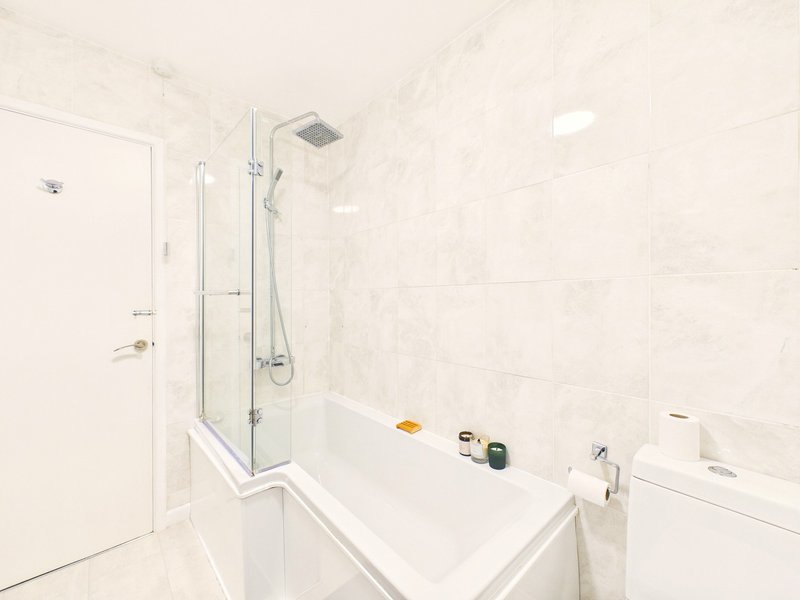 Modern bathroom with white tiles, glass shower enclosure, bathtub and sink