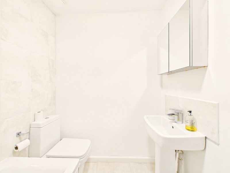 Clean white bathroom with toilet, pedestal sink, mirror cabinet and bathtub