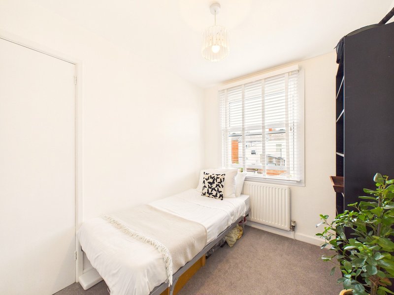 Bright bedroom with single bed, window with shutters, radiator and potted plant
