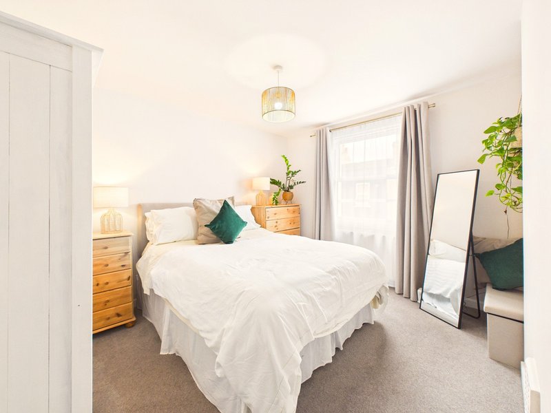 Bright bedroom with double bed, white bedding, wooden nightstand, mirror and potted plants