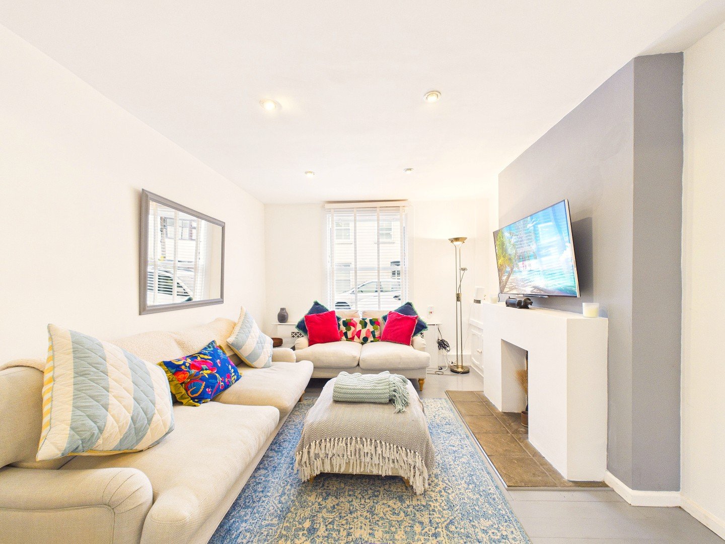 Modern living room with cream sofa, colorful cushions, TV on wall, and wooden flooring