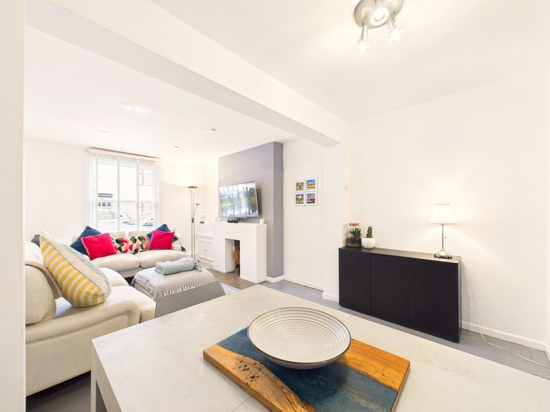 Modern open-plan living space with cream sofa, bed with colorful cushions, wooden coffee table, and wall-mounted TV