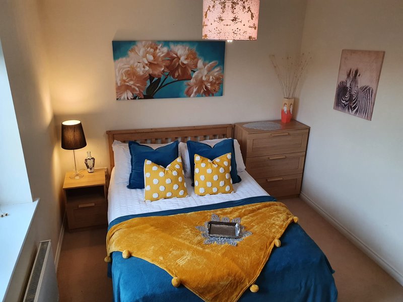Bedroom with double bed, blue and yellow bedding, wooden furniture and wall art