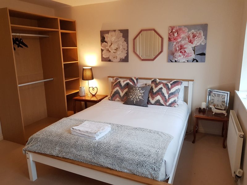 Bedroom with white bed, wooden wardrobe, bedside lamps and floral wall art
