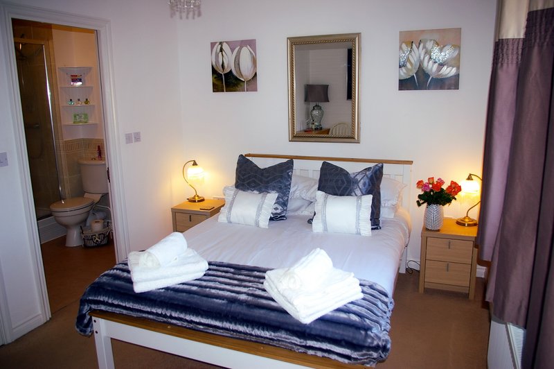 Bedroom with double bed, navy bedding, two bedside lamps, mirror above headboard, and framed wall art