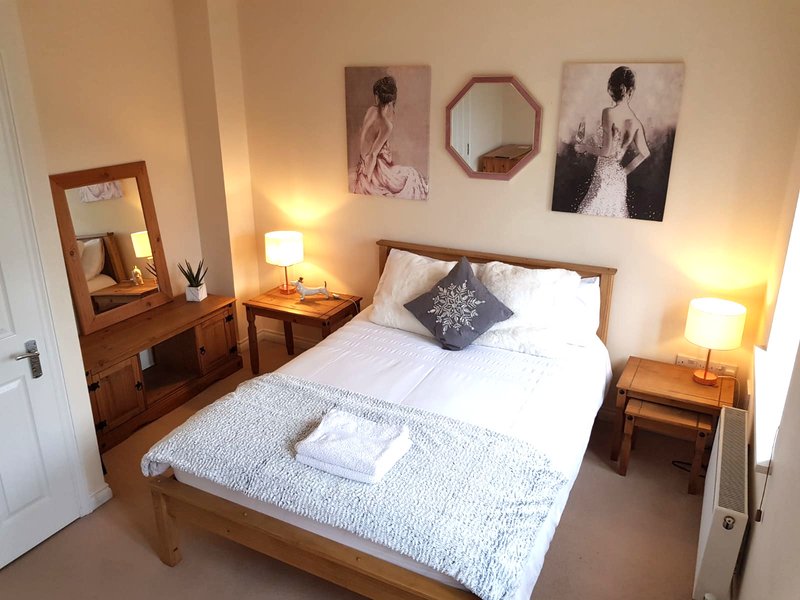 Bright bedroom with double bed, wooden furniture, wall art, and bedside lamps