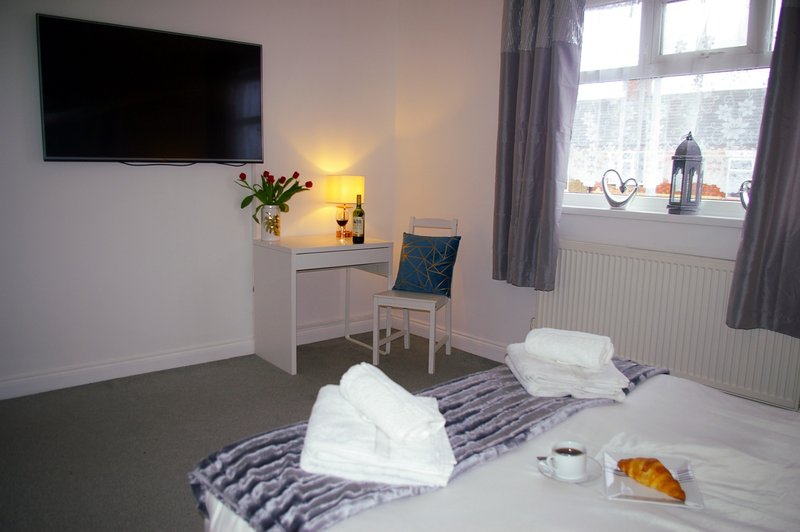 Modern bedroom with double bed, white towels, wall-mounted TV, desk and window with garden view