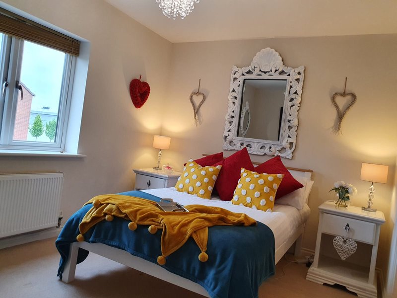 Bright bedroom with double bed, colorful pillows, decorative mirror, bedside lamps and window