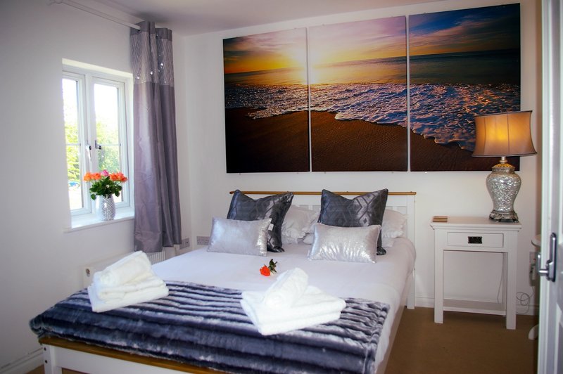 Bright bedroom with double bed, sunset wall art, bedside lamp and flowers on windowsill
