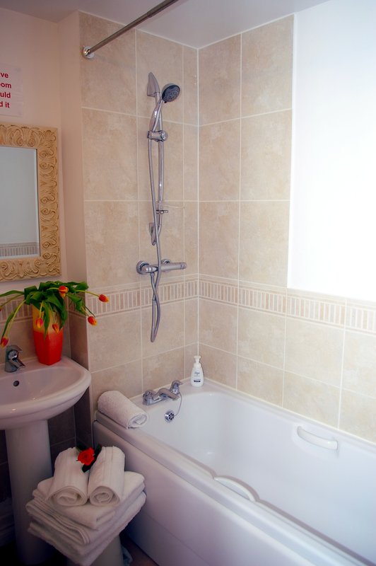 Bathroom with beige tile walls, bath tub, pedestal sink, mirror and shower fixtures