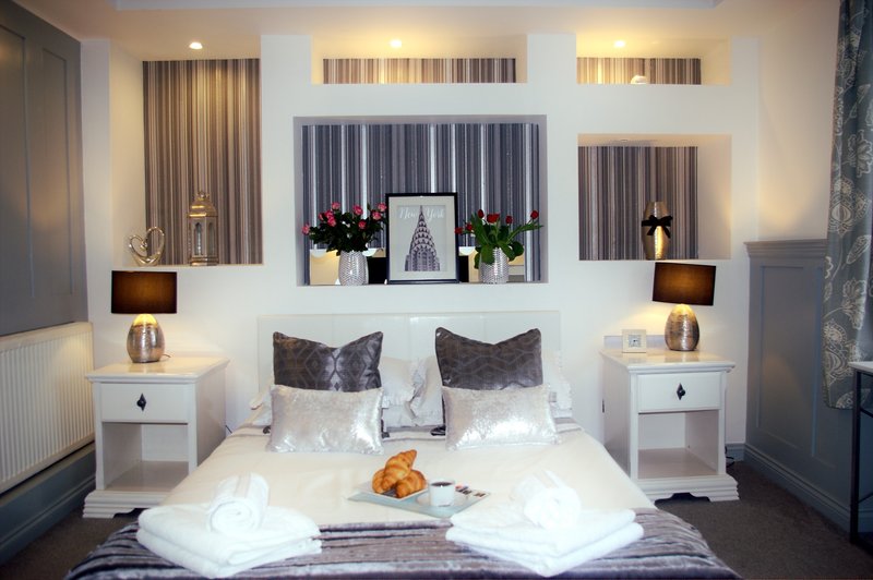 Modern bedroom with double bed, white bedding, dark cushions, and symmetrical nightstands with lamps