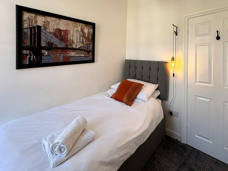 Bedroom with single bed, grey headboard, framed wall art, pendant lights and white door