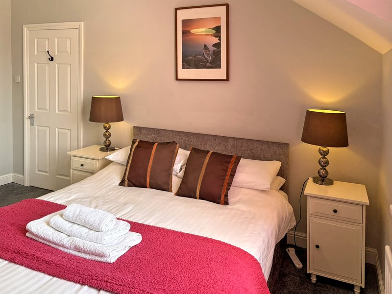 Bedroom with double bed, pink bedspread, brown cushions, bedside tables with lamps