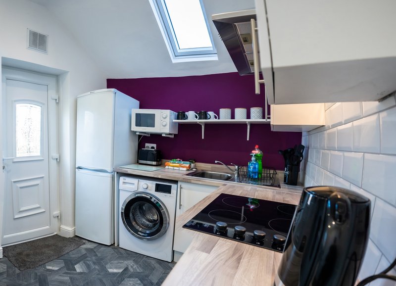 Kitchen with white appliances, washing machine, purple accent wall, skylight and wooden worktop