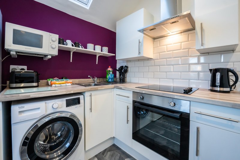 Modern kitchen with white cabinets, purple accent wall, integrated appliances and subway tile backsplash
