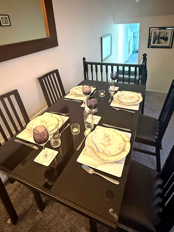 Dining room with dark table set for four, wooden chairs, and crib visible in background