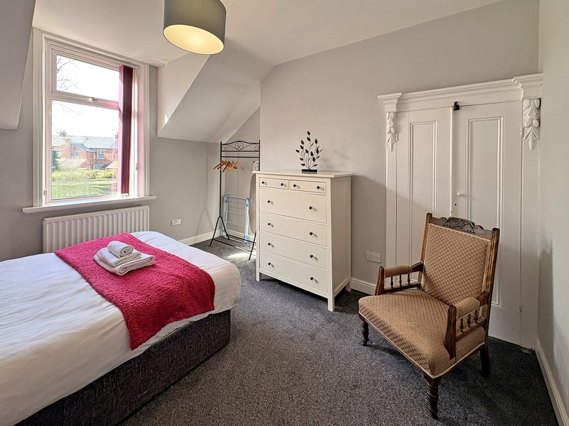 Bright attic bedroom with single bed, white dresser, armchair and window overlooking countryside