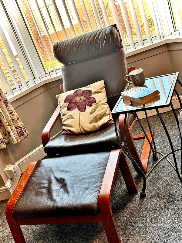 Black leather armchair with cushions, footrest, and side table near window