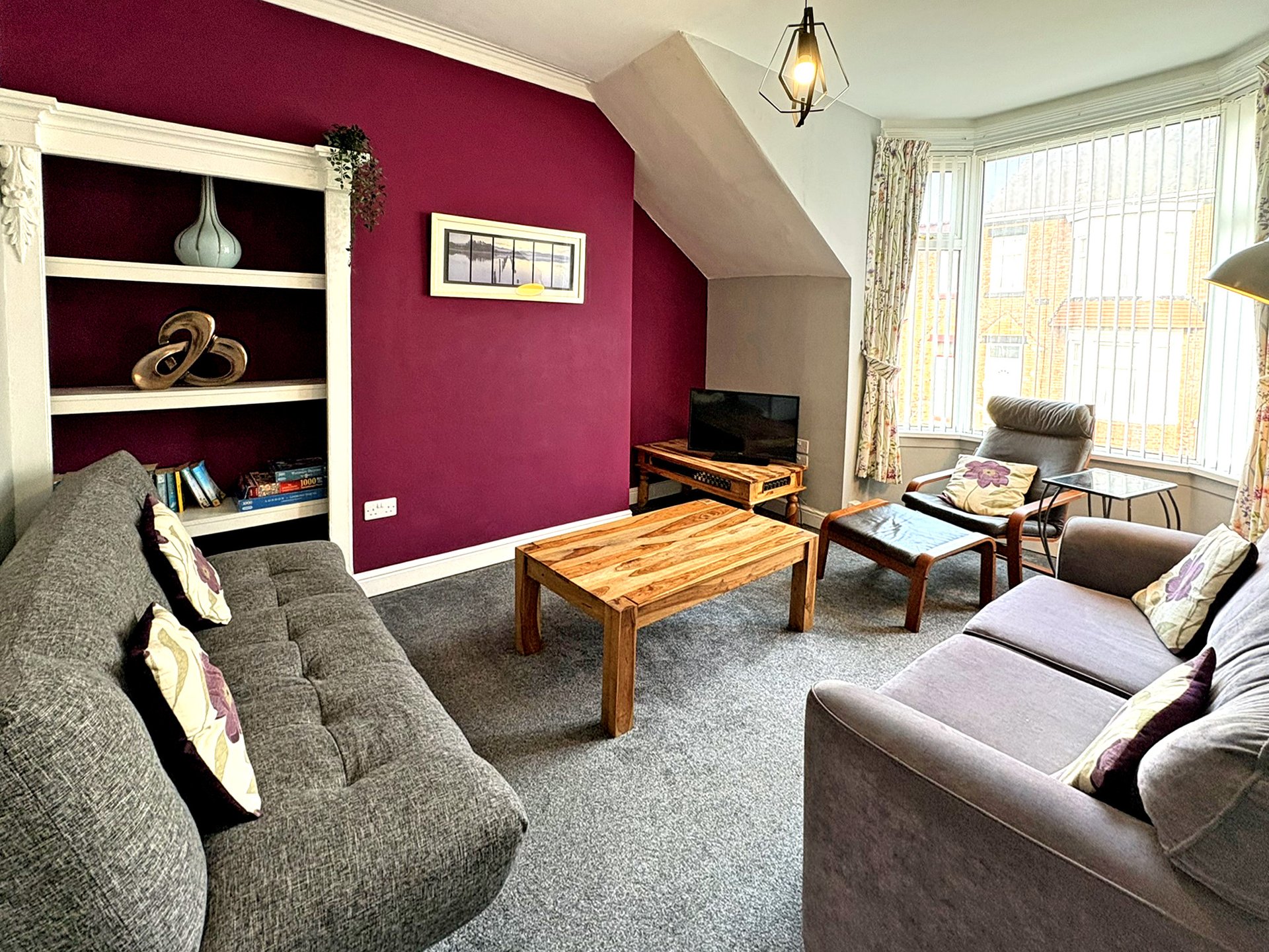 Spacious living room with purple accent wall, curved grey sofa, wooden coffee table and built-in shelving