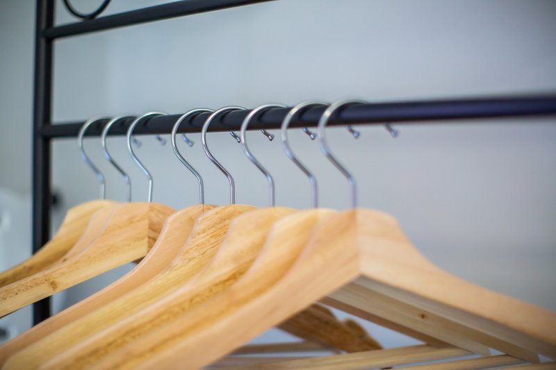 Wooden coat hangers hanging on a metal rail against white wall