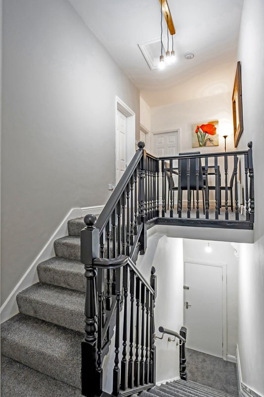 Staircase with gray carpet, black metal railings, and white walls leading to upper landing