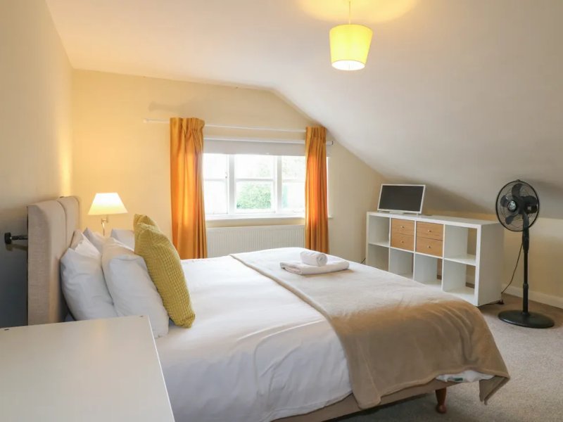 Bright attic bedroom with double bed, white linens, golden cushion, storage shelving and fan