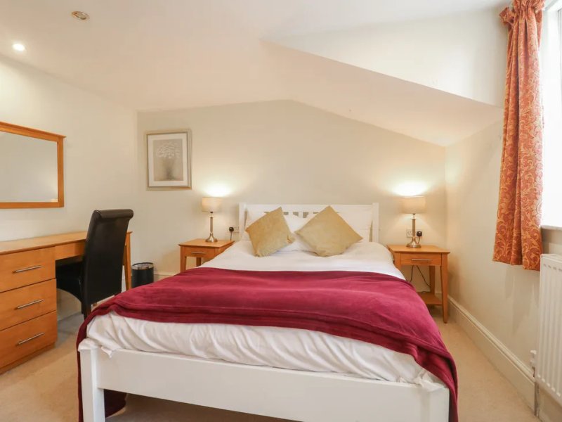 Bright attic bedroom with double bed, burgundy throw, wooden furniture and desk area