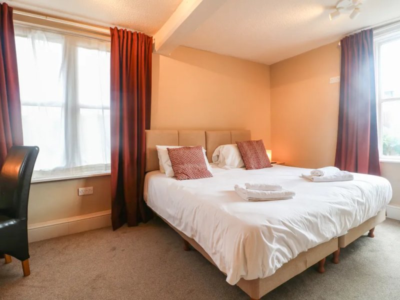 Bright bedroom with double bed, red curtains, windows and beige walls