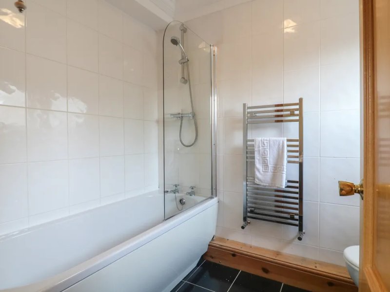 Modern bathroom with white subway tiles, bathtub with glass shower screen, heated towel rail and wooden accents