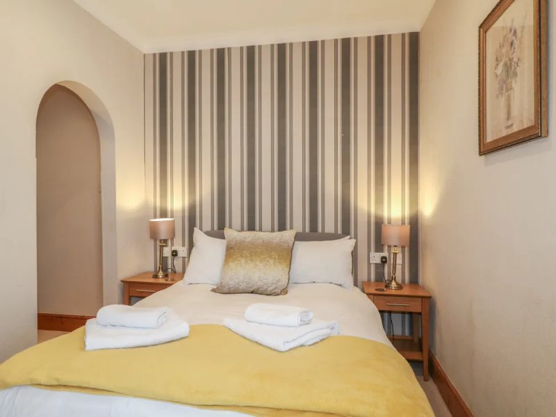 Bedroom with yellow bedding, striped headboard, bedside tables, lamps and framed wall art