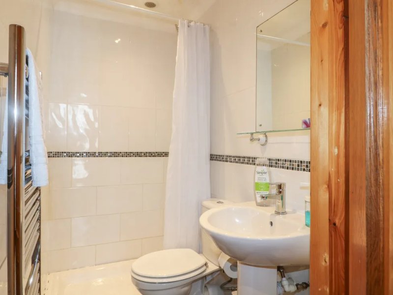 Clean bathroom with white tiles, round sink, toilet, shower cubicle and mirror