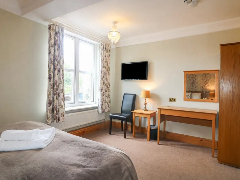 Bright bedroom with double bed, wooden desk, TV, and window with patterned curtains