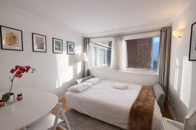 Bright bedroom with double bed, white bedding, brown throw, framed wall art and windows