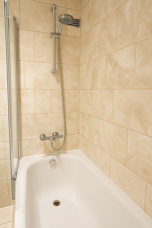 Bathroom with white bathtub, beige tile walls, and chrome shower fixtures