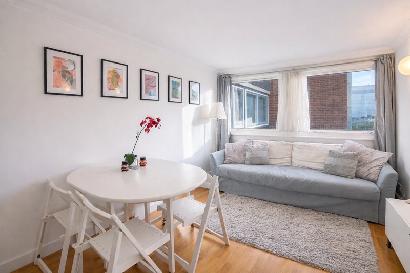 Open-plan living and dining area with round white table, sofa, framed wall art and brick exterior views