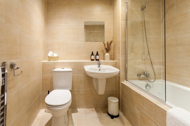 Modern bathroom with beige tiles, pedestal sink, toilet, bathtub and glass shower enclosure