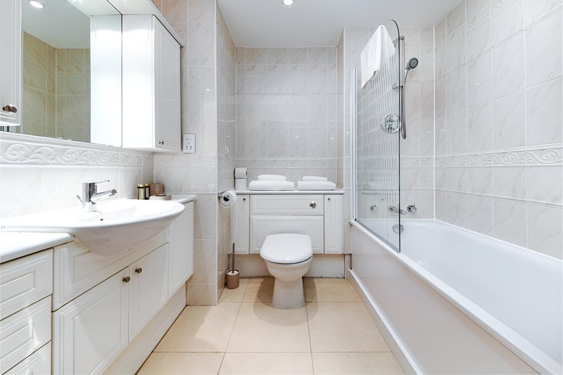 Modern bathroom with white vanity, toilet, bathtub with shower screen and tiled walls